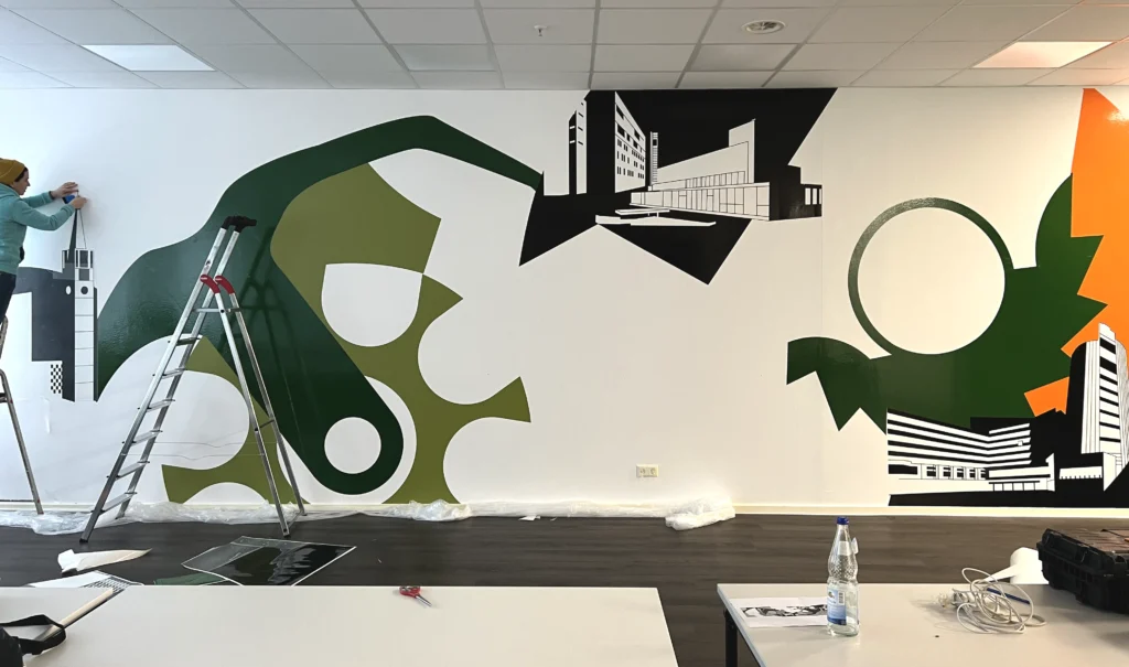 Foto aus dem Prozess der Wandgestaltung. Die Hauptelemente in Grün befinden sich bereits an der Wand, der Rest wird nachträglich angebracht.